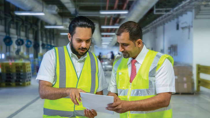 Two Oman Cargo men in safety vests reviewing documents